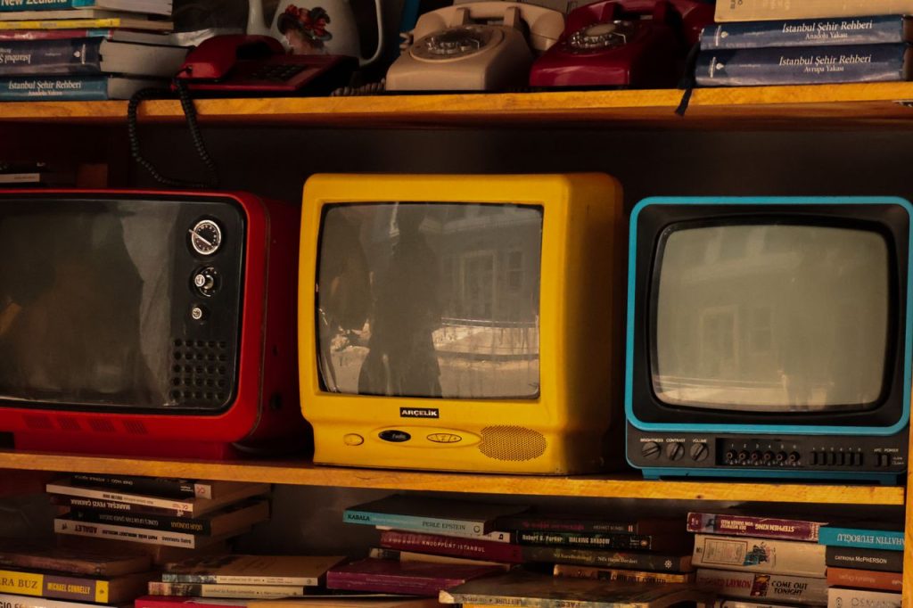 Three colourful vintage television sets on a wooden shelf